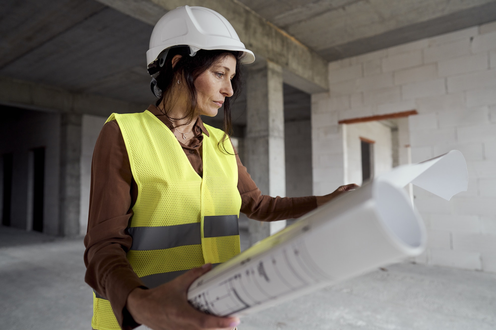 Female mature caucasian engineer standing on construction site and browsing building plans
