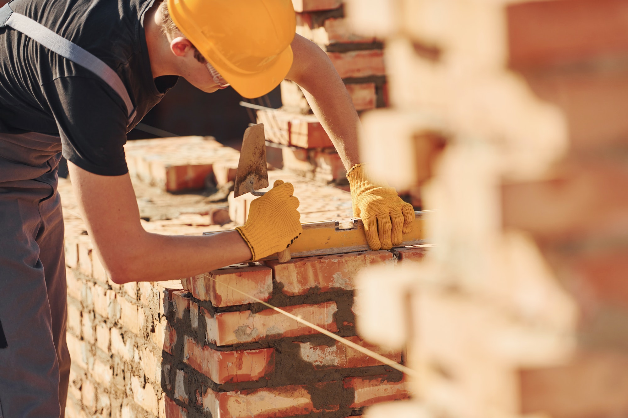 Measures of brick wall. Construction worker in uniform and safety equipment have job on building Measures of brick wall. Construction worker in uniform and safety equipment have job on building