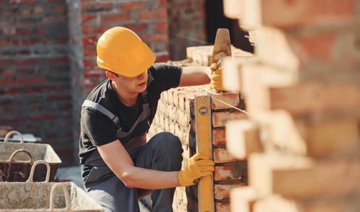 Measures of brick wall. Construction worker in uniform and safety equipment have job on building