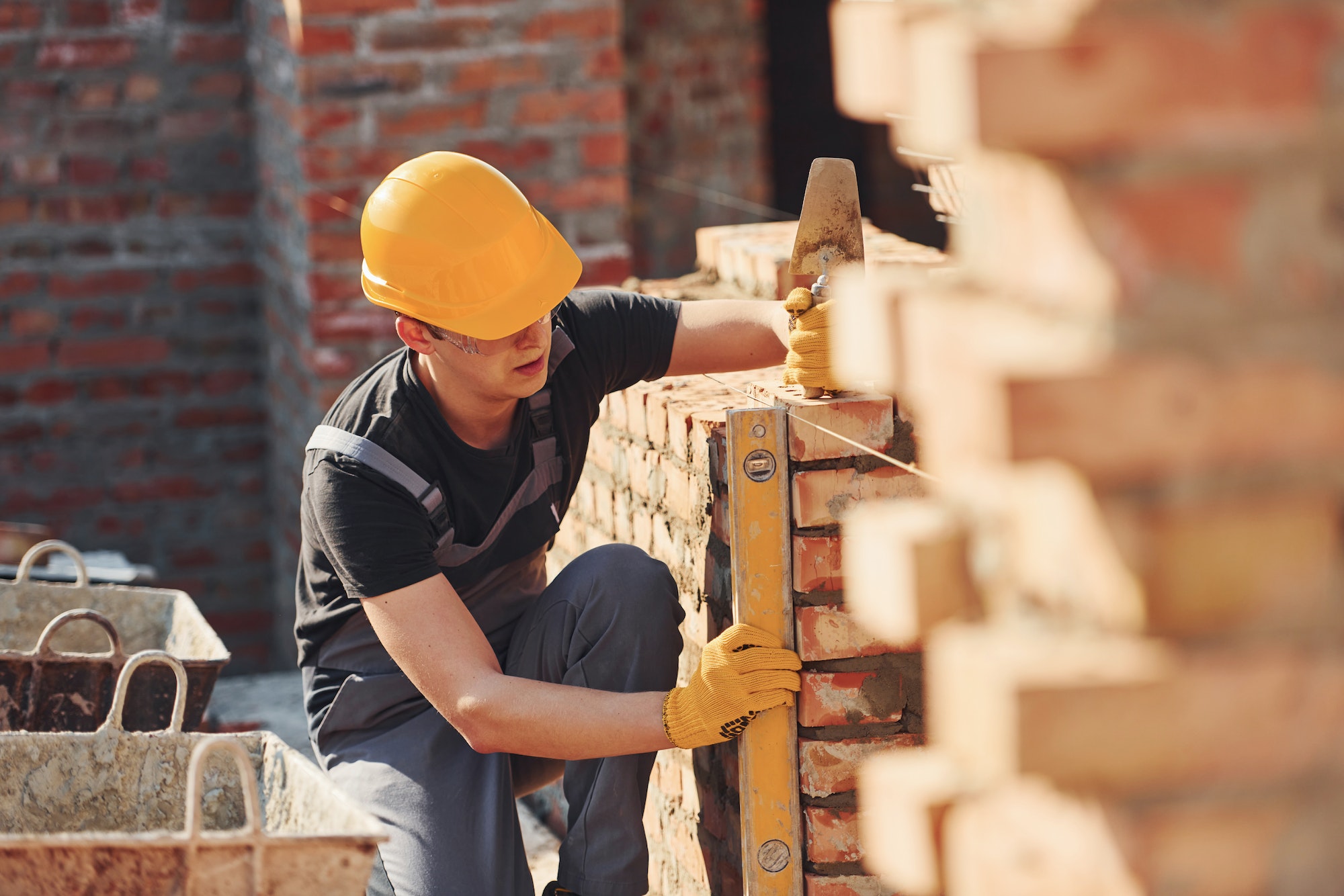 Measures of brick wall. Construction worker in uniform and safety equipment have job on building