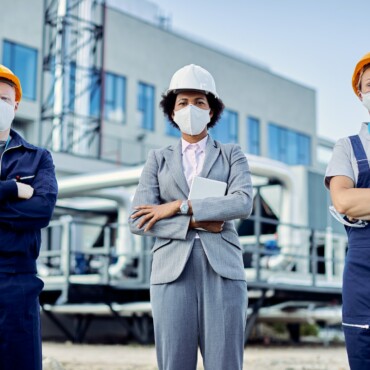 Team of confident civil engineers with protective face masks and construction site.