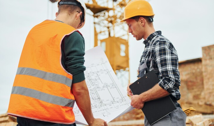 Two construction workers in uniform and safety equipment have job on building together