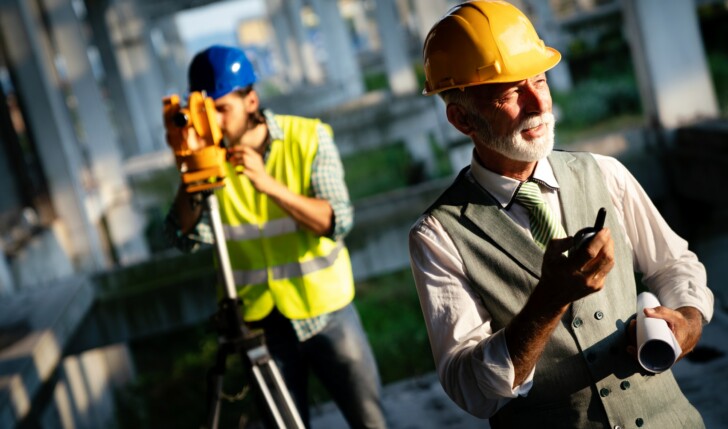 Two satisfied engineers talking at building site with construction structure in background